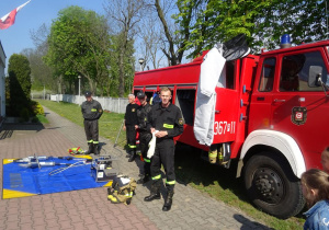 Strażacy prezentują narzędzia pracy strażaka znajdujące się w wozie strażackim.